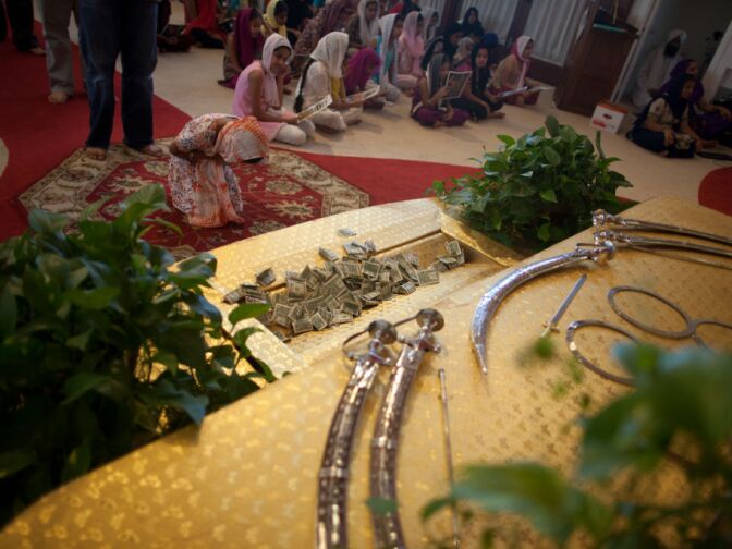 A woman bows after offering a donation in front of the Sikh holy book during prayers at the Khalsa Care Foundation.