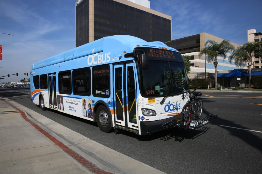 An OC Bus has a blue top and a bicycle on the rack in front.