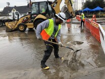 An LADWP worker shovels mud after a water main break floods residential streets in South LA.