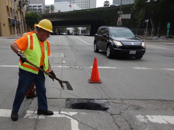 Los Angeles city worker Hugo Vasquez shovels asphalt into a pothole.
