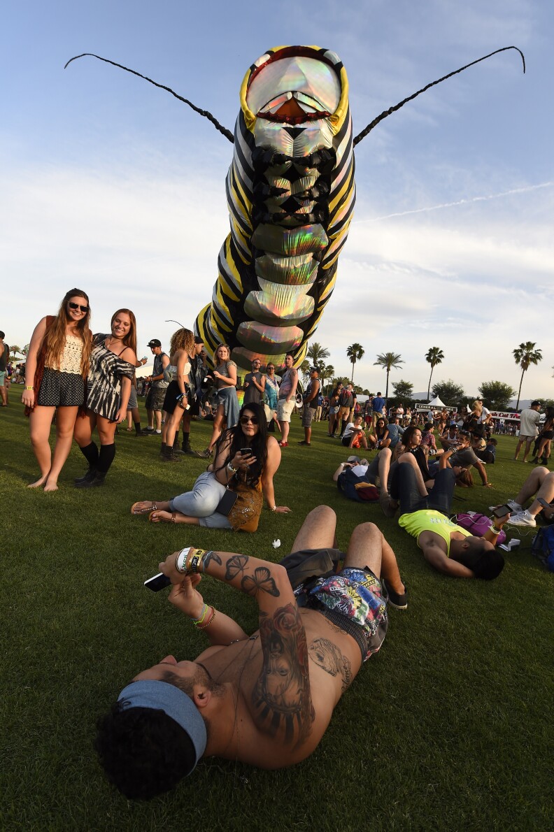 A man takes a photo of two girls against the back drop of a giant caterpillar on the first day of the Coachella Music Festival, in Indio, California, April 10, 2015.  AFP PHOTO / ROBYN BECK        (Photo credit should read ROBYN BECK/AFP/Getty Images)