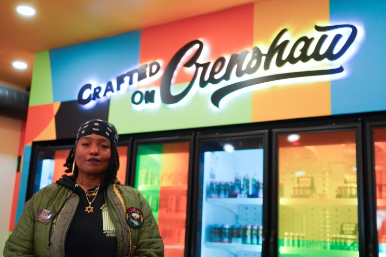 Kika Keith poses for a photo at her dispensary, Gorilla RX, in South L.A. on May 1, 2025. Cannabis infused drinks fill a row of colorful refrigerator doors behind her.
