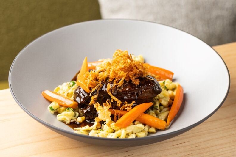 A plate of German spaetzle, which is rolled up pieces of yellow dough that can be cooked like pasta. There's a cooked piece of brown meat covered with sauce and slivers of carrot.
