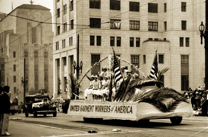 Crowds watch on as a float of female garment workers representing the United Garment Workers of America travels down Spring Street. The Los Angeles Times Building is present in the background, at Spring and First Street. Photo dated: September 7, 1936. 