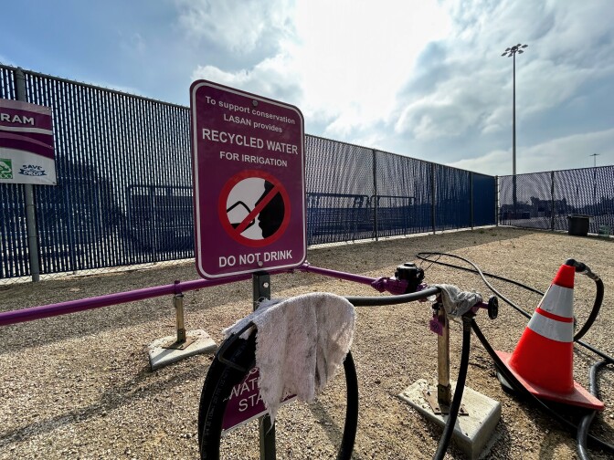 A purple sign outside by pipes that says to support conservation LASAN provides recycled water for irrigation. Do not drink.