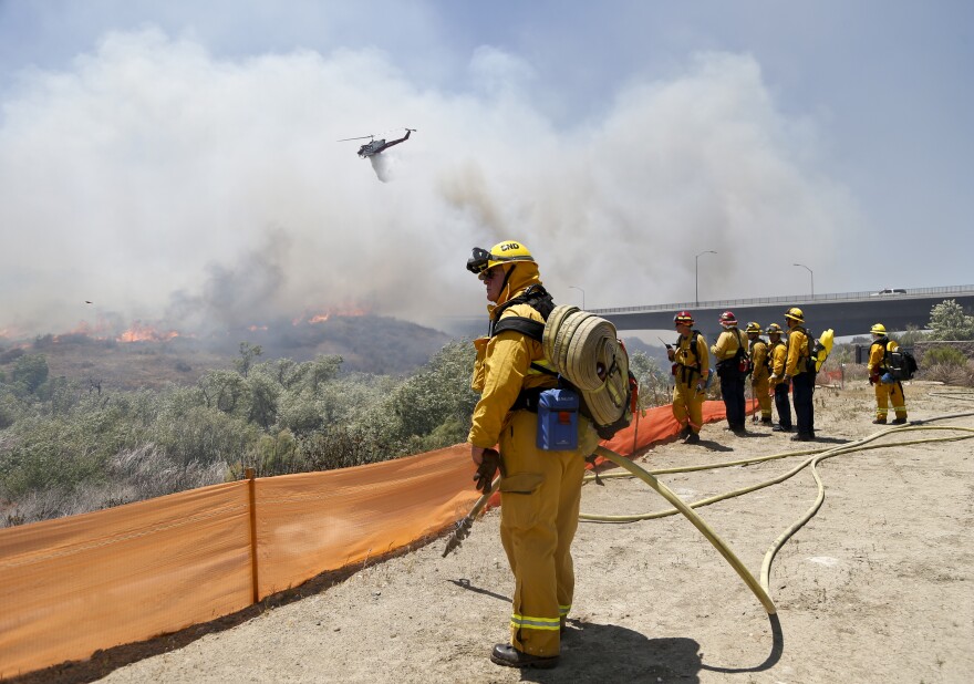 Firefighters watch from a ridge as a helicopter drops retardant on a out-of- control wild fire Tuesday, May 13, 2014, in San Diego.