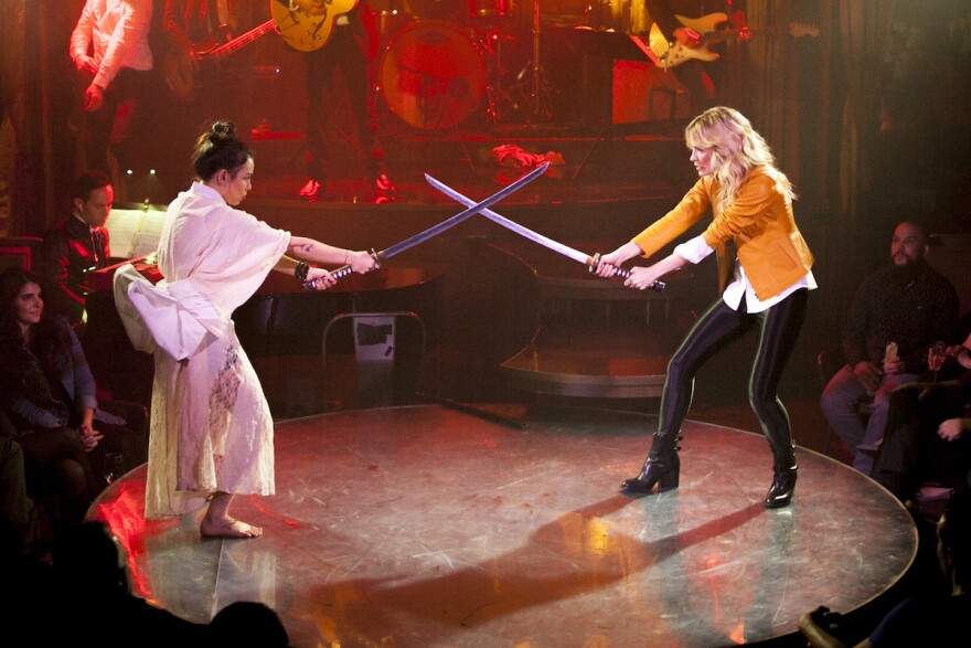 An image of two actresses pretend to fight with metal swords, re-creating a scene from Quentin Tarantino's movie "Kill Bill."