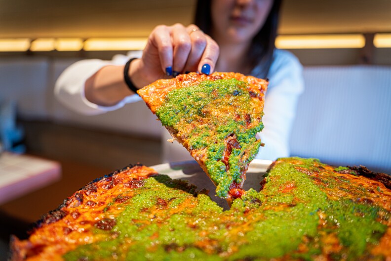 A person with painted blue fingernails grabs a slice of pizza.
