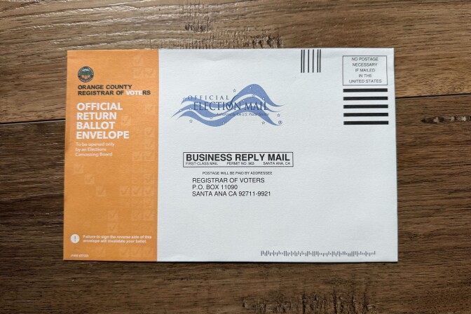 A close-up of a ballot return envelope from Orange County. The left side is orange and reads "Official Return Ballot Envelope."