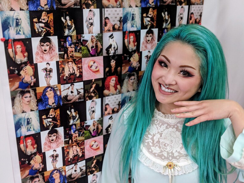 Amy Doan, founder of the makeup brand Sugarpill, poses in front of a backsplash that features different pictures of drag queen Laila McQueen.