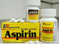 A box of aspirin and two bottles of aspirin, with several pills on top and in front of the box. 