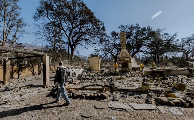 The charred remains of what used to be the interior of a home, with a stone fireplace sticking out from the rubble.