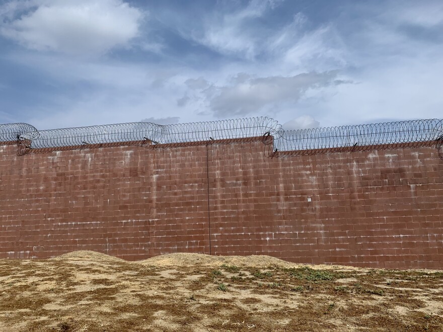 A brick wall with barbed wire on a hilly place and with a blue, cloudy sky on the background.