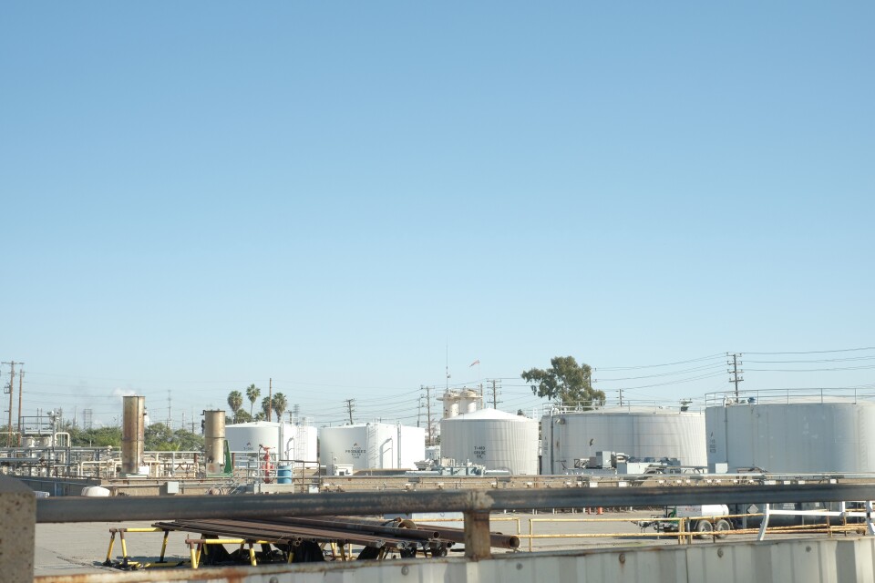 Large white oil storage tanks in a cement yard with blue skies. 