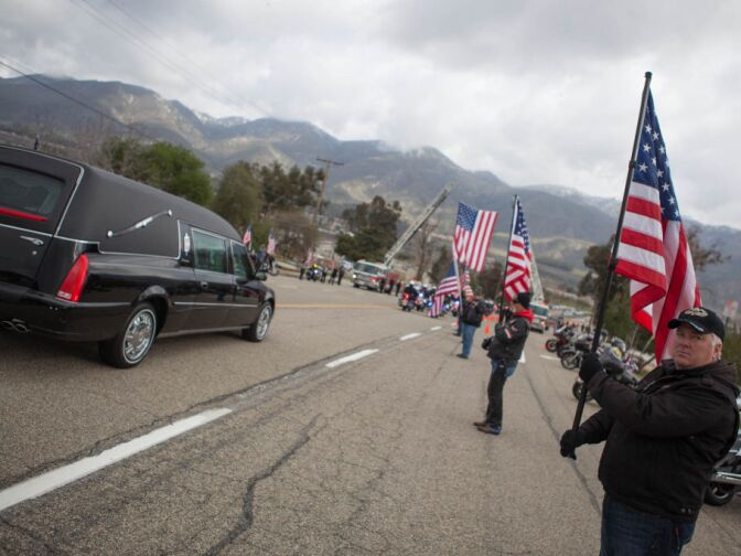 Members of a motorcycle club hold flags in salute of fallen San Bernardino Sheriff's Det. Jeremiah MacKay outside the entrance to San Miguel Amphitheater on Feb. 21, 2013.