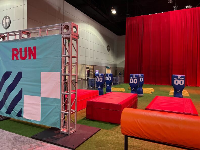 A kids' activity station were children can practice football skills includes several tackling dummies with jerseys and raised platforms. A large sign that reads Run is at the entrance to the activity station.
