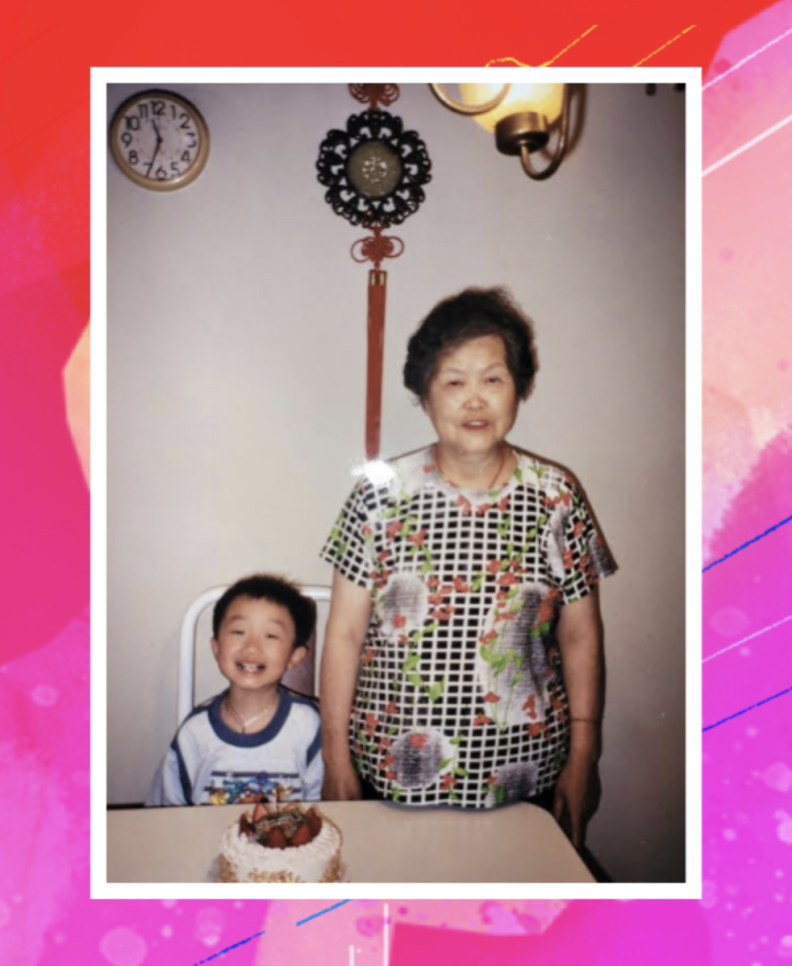 Photo shows a smiling little boy, left, with a woman with short dark hair who is wearing a printed dress. They're behind a table that has a cake with candles on it.