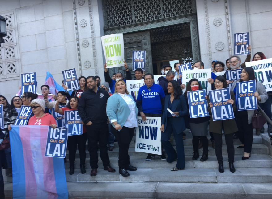 A crowd of people on the steps of a public building holding signs that read "ICE Out of LA!"