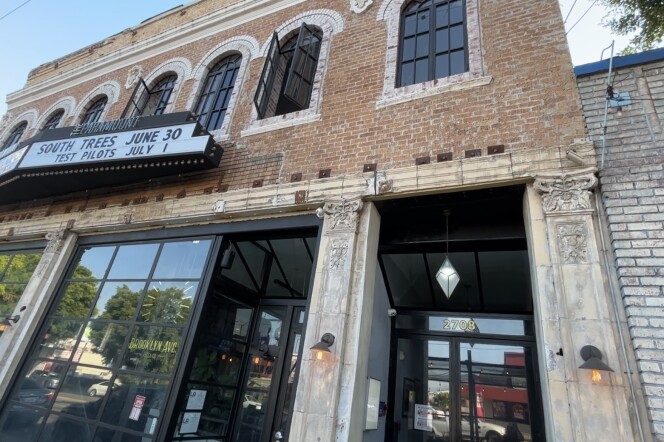 An image of the outside of an old brick two-story building with large glass windows on the first floor. 