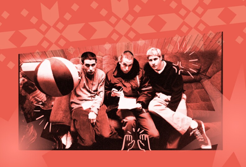 A black and white photo of three men sitting on a couch. One man is holding a basketball up to the camera.