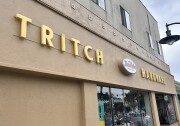 The exterior of a tan, two-story building on a partly-cloudy afternoon. The words "Tritch Hardware" are displayed across the front in yellow, with a smaller pop-out sign in between that reads "True Value" in red.