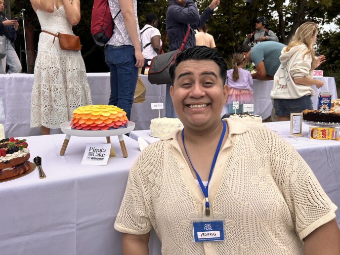 A person smiling in front of a multi-color cake.