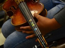 Some of the students' violins have stickers to mark finger positions to help them remember the notes.