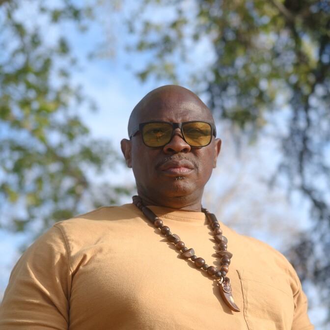A man wearing a gold t-shirt and a large craft necklace 