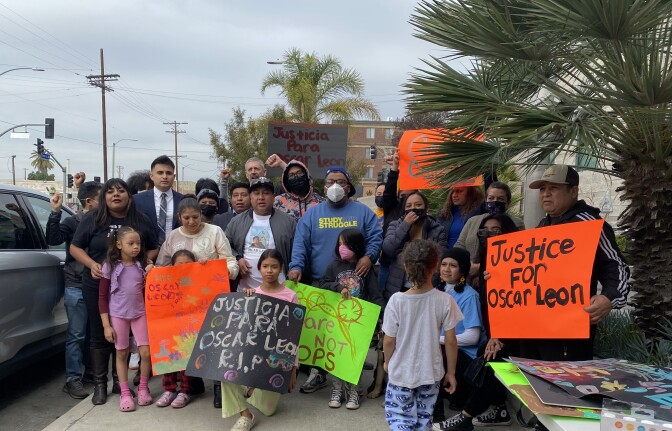About two dozen organizers and family of Oscar Leon Sanchez stand together. Several hold signs which are bright green and orange. Signs read "Justice for Oscar Leon" 