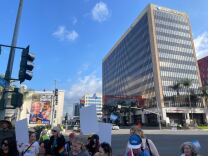 About a dozen people stand on a street corner holding LGBTQ and trans pride flags.