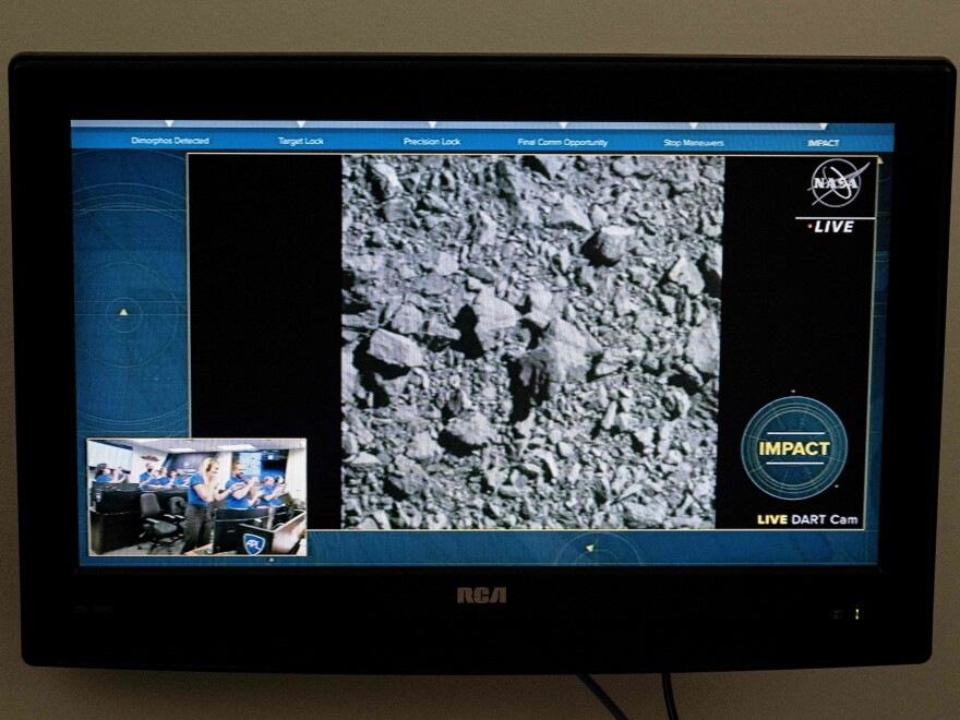 An RCA TV screen shows a rocky gray image. There's a NASA logo in the corner with the word LIVE underneath, footage of a control room in the lower left picture-in-picture. In the lower right, it says "IMPACT" and "LIVE DART Cam."