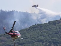 A plane and helicopter work to douse the flames of a fire burning on a mountainside 