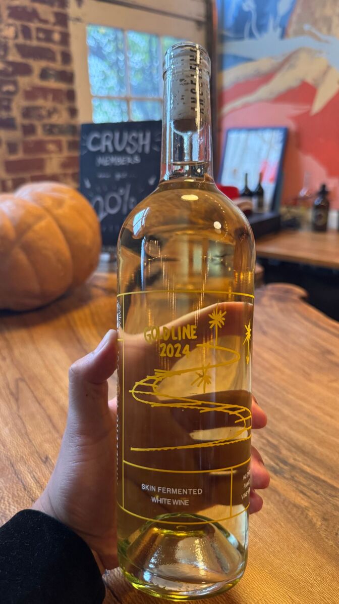 A wine bottle with bright yellow wine in it that says "Gold line 2024".