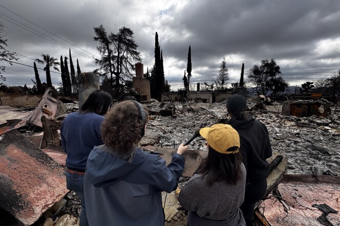 Four people stand atop the rubble of an Altadena home.