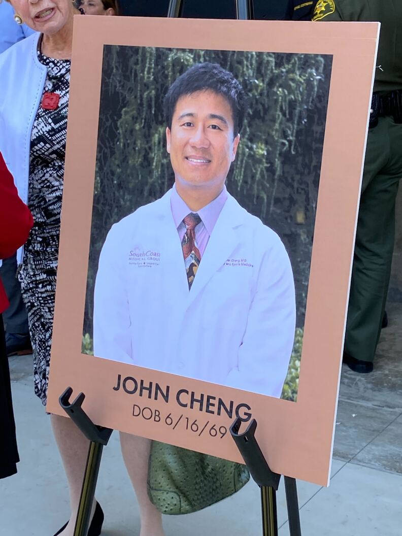 A posterboard-sized photo propped up on an easel shows a doctor wearing a lab coat. The photo is captioned John Cheng, DOB 6/16/69