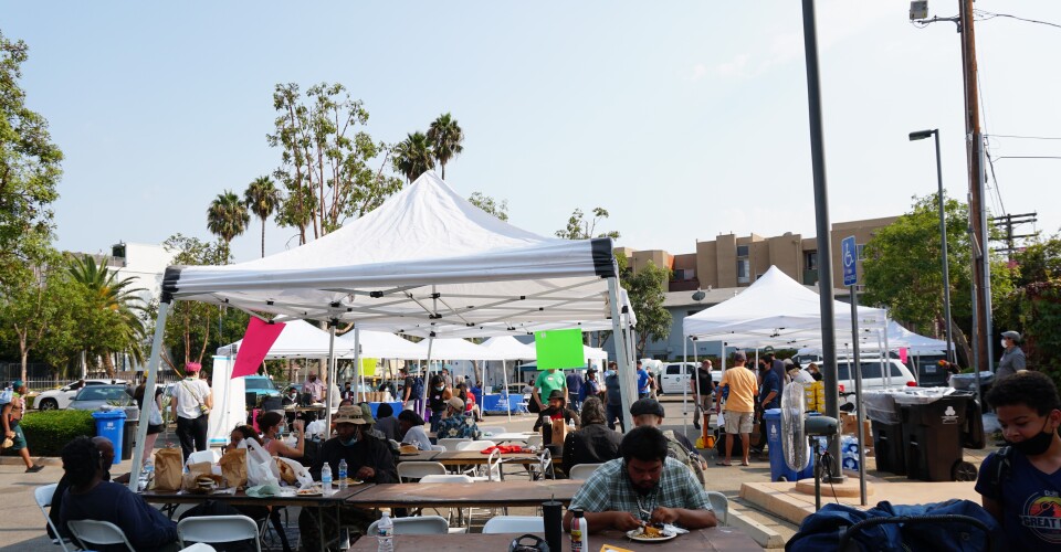 outside of the durant branch of the library, tents are set up over tables for unhoused people. Volunteers are helping.