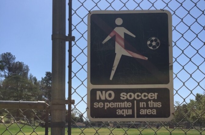 A sign on a fence that says "no soccer in this area/se permite aquí. A symbol of someone kicking a ball is also on it.