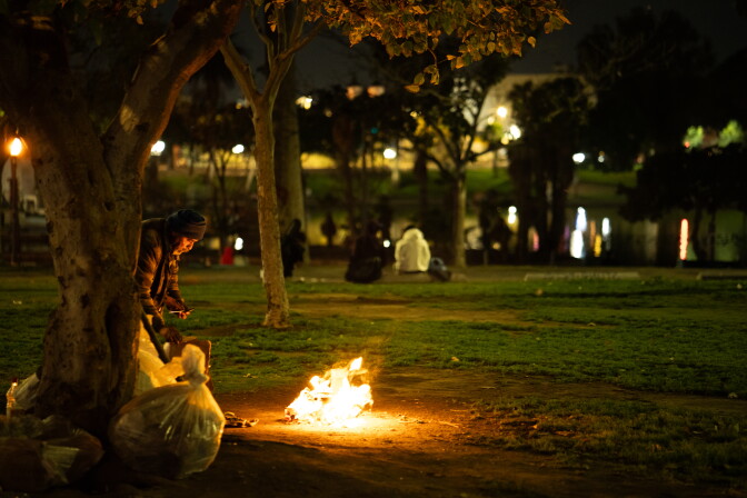 A man stands in front of a fire in a public park as other people sit on benches in the background.