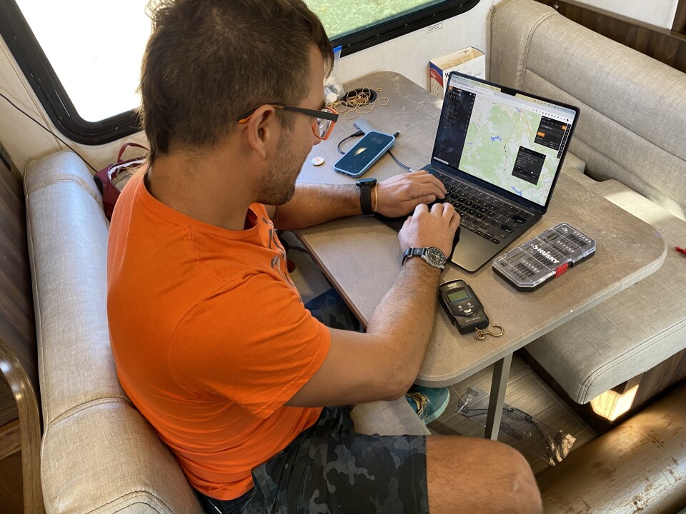 A man with light-tone skin works on a laptop computer at an RV dining table.
