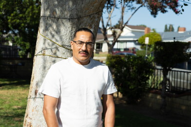 A man stands in front of a tree in a residential neighborhood.