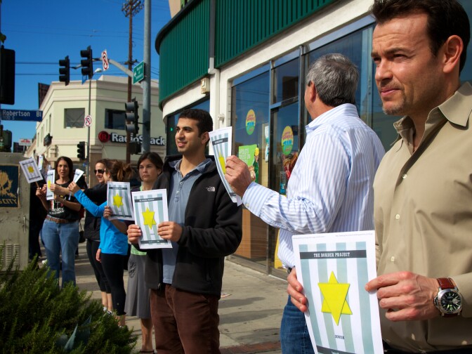 Several participants stand on the corner of Pico and Robertson holding up concentration camp insignias.