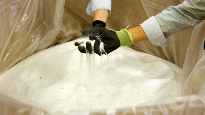 A person holds a handful of fine powder that is sifting through their gloves 