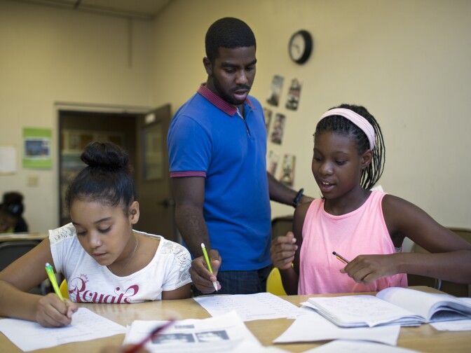 Teaching assistant Jonathan Curtiss checks the work of Alyse Wilson, 11, left, and Kayla White, 12, during the fourth week of a pre-algebra class at the West Angeles Church Youth Center on Thursday afternoon, July 30, 2015.