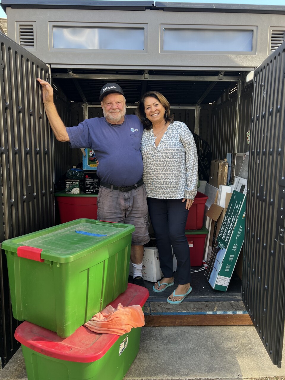 A couple stand in a shed surrounded by red and green storage boxes. 