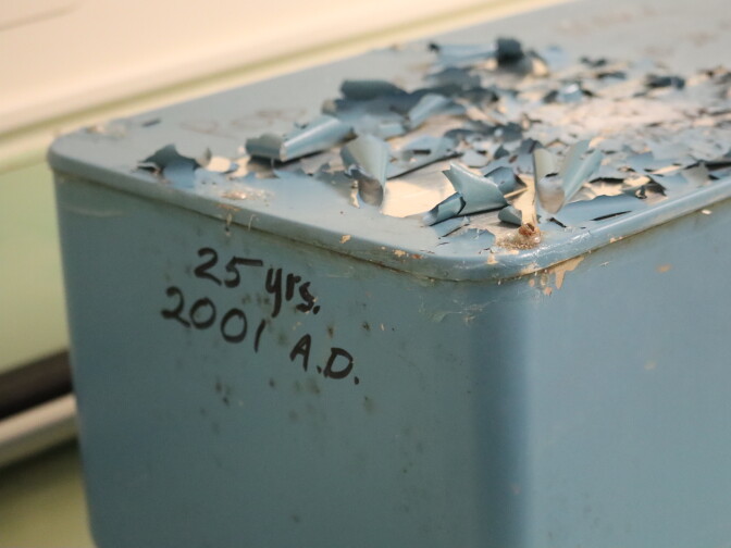 A faded and peeling blue metal box with the words "25 yrs. 2001 A.D." written on the front in black marker.