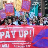 Protesters display banners for equal pay.