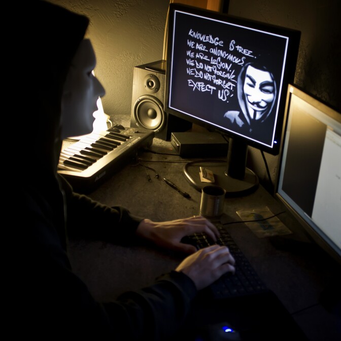 A masked hacker, part of the Anonymous group, hacks the French presidential Elysee Palace website on January 20, 2012 near the eastern city of Lyon. Anonymous, which briefly knocked the FBI and Justice Department websites offline in retaliation for the US shutdown of file-sharing site Megaupload, is a shadowy group of international hackers with no central hierarchy. On the central screen, an Occupy mask is seen.