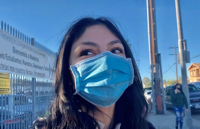 A close up photo of the face of a young woman in a sweatshirt and mask.