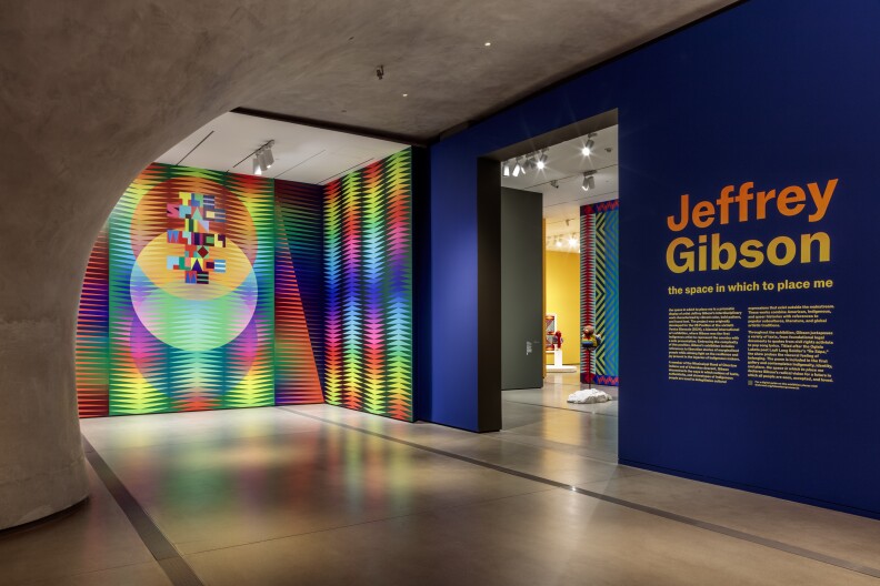 The entrance to the Jeffrey Gibson exhibit at The Broad museum includes a blue wall with the artist's name and a multicolored artwork.