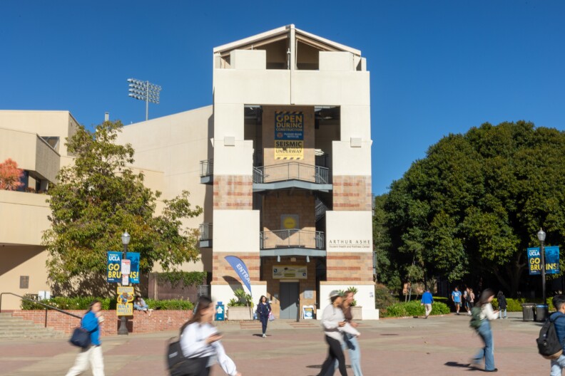 A large brick and white building stands in the background of a large concrete courtyard that many students walk on.